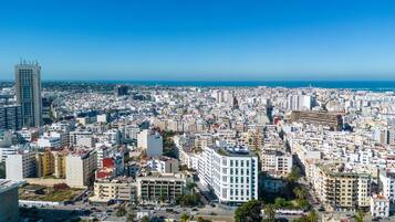 A cityscape with a mix of high-rise and mid-rise buildings, a clear blue sky, and a view of the sea.