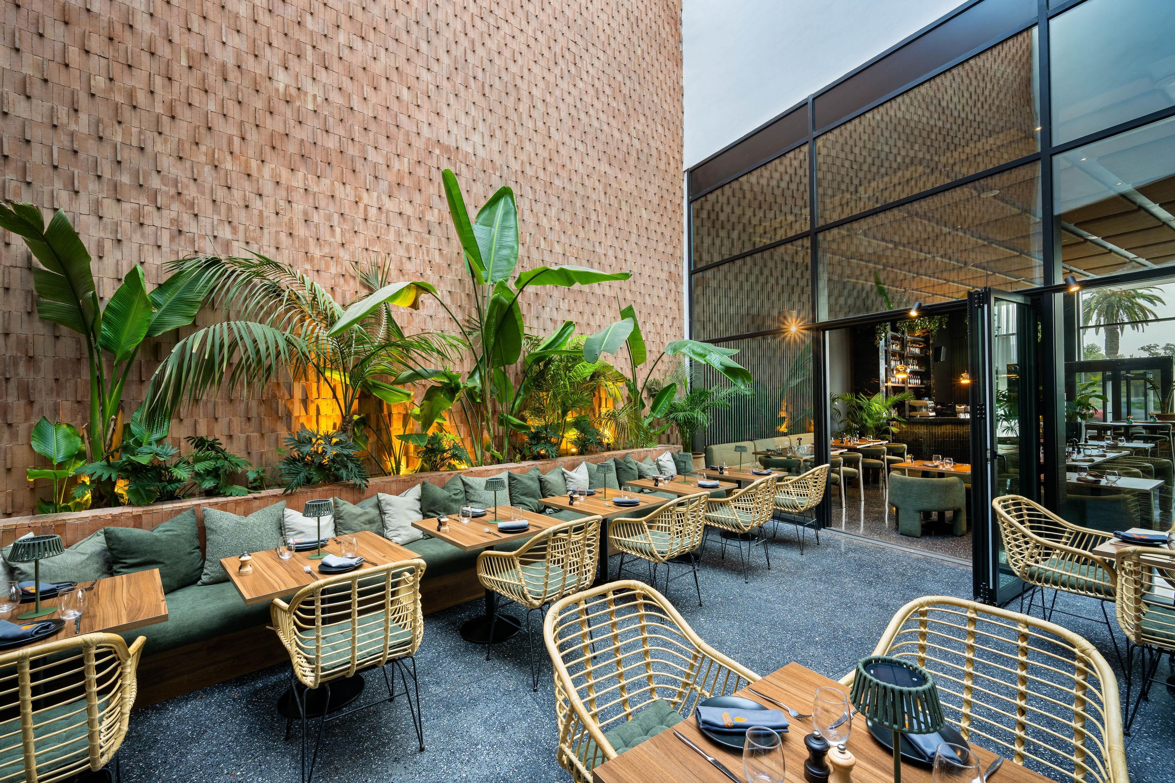 An outdoor seating area with tables and chairs, surrounded by lush greenery and a brick wall.