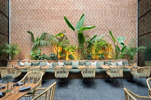 A restaurant with a brick wall backdrop, green cushioned seating, and wicker chairs. - Radisson Hotel Casablanca Gauthier La Citadelle (Casablanca)