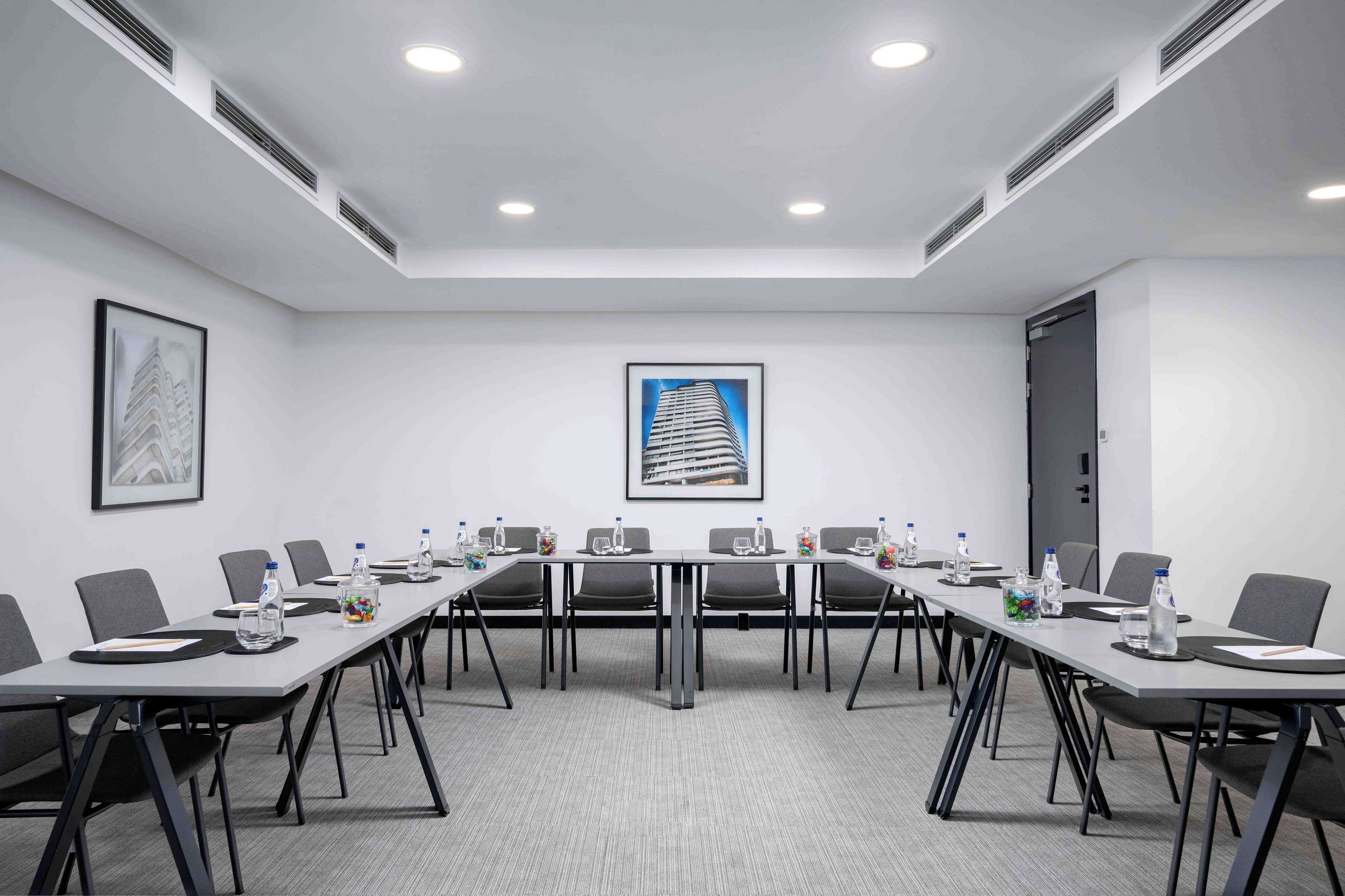 A conference room with a long table, chairs, water bottles, and framed pictures on the walls.