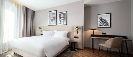 A hotel room with a large bed, a desk with a chair, and two wall-mounted lamps.
