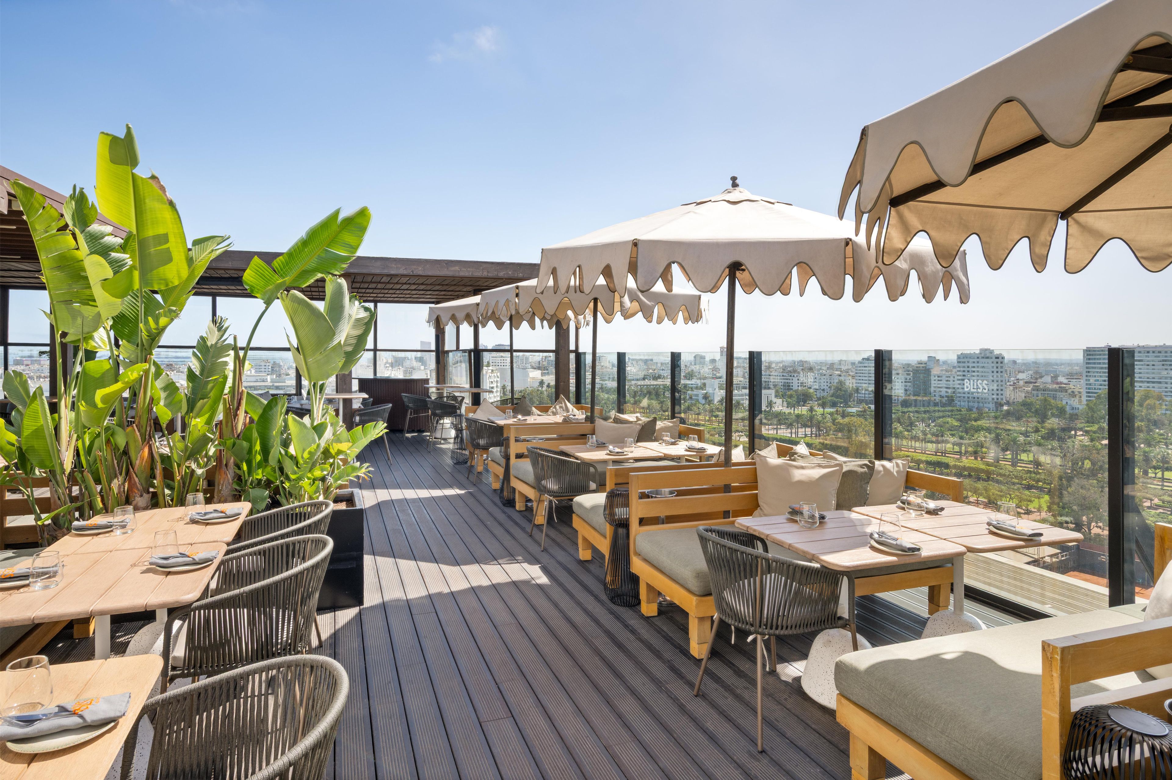 An outdoor dining area with tables and chairs, large umbrellas, and tropical plants.