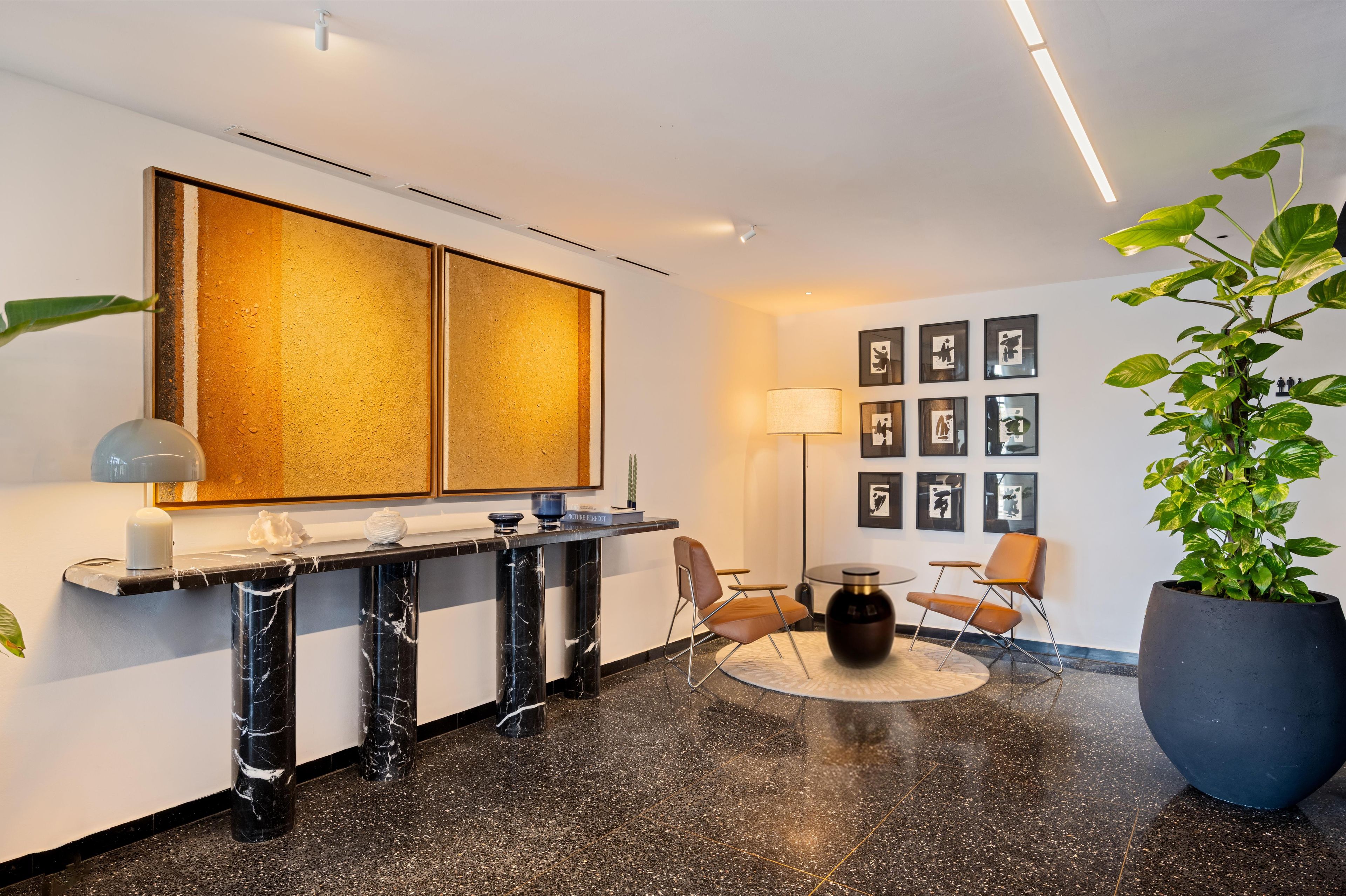 A modern lobby with a marble reception desk, a large abstract painting, a floor lamp, and a potted plant.