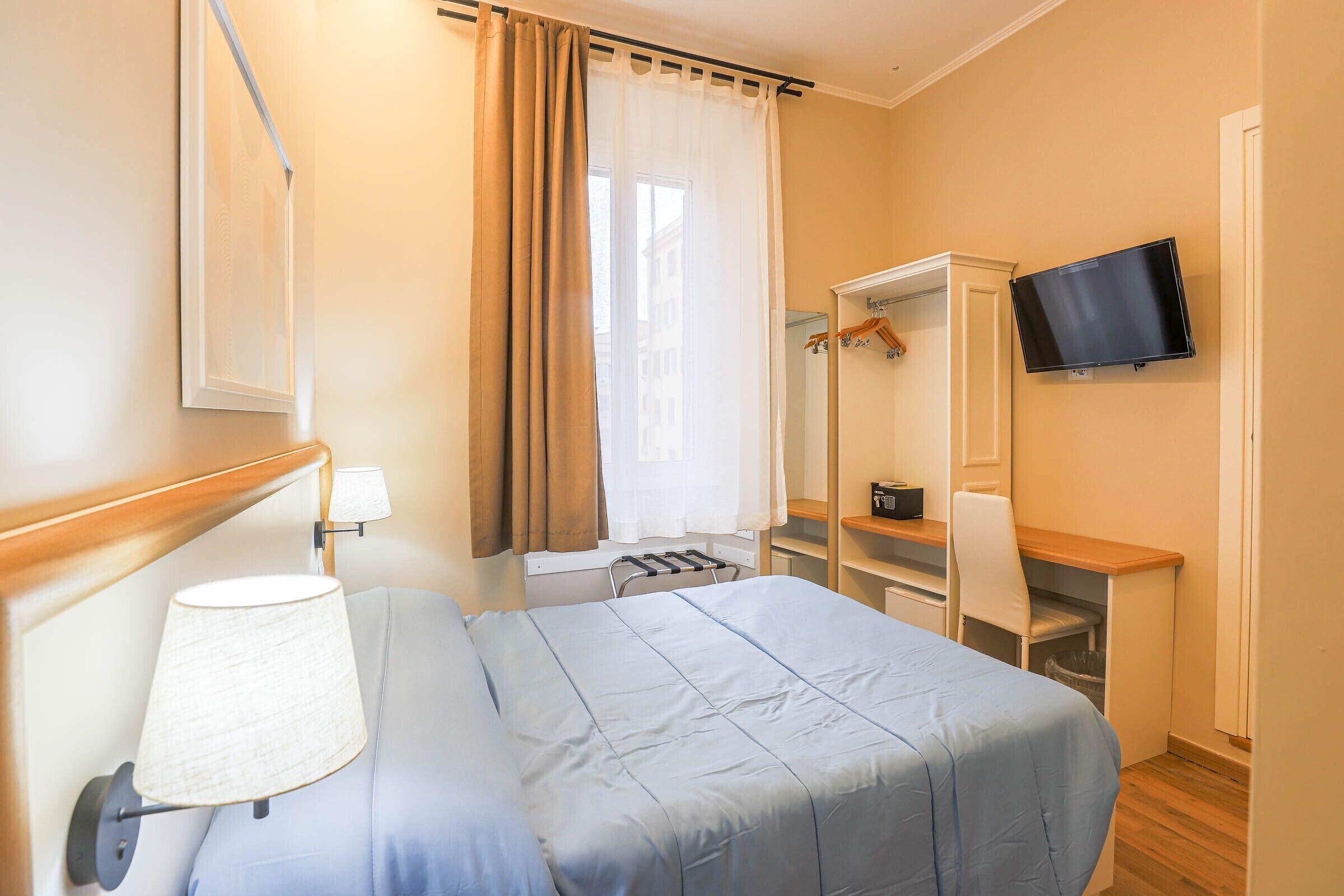 A hotel room with a bed, a desk, a chair, a television, and a wardrobe.