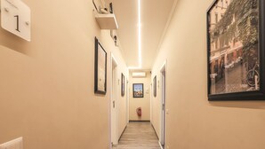 A hallway with a wooden floor, beige walls, and framed pictures. There is a fire extinguisher on the wall and a light fixture above. - Binaro 0 a Termini (Rome)