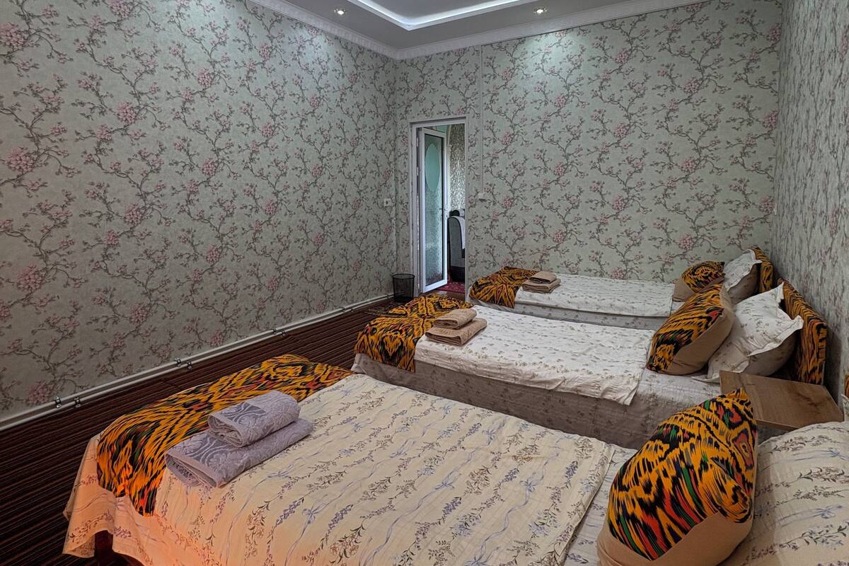 A hotel room with two beds, floral wallpaper, a wooden floor, and a ceiling light.