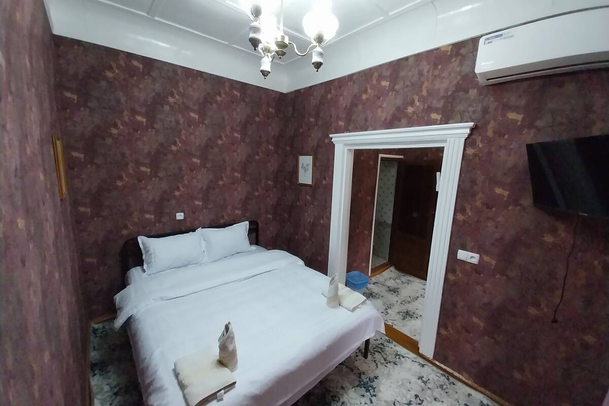 A bedroom with a bed, a chandelier, an air conditioning unit, and a television.