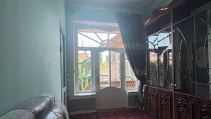 A room with a leather sofa, a patterned carpet, a wooden cabinet, and a window with curtains. - Fayz Guest House (Samarkand)
