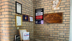A brick wall with a sign indicating breakfast hours, a guest house sign, and various framed certificates. - Fayz Guest House (Samarkand)