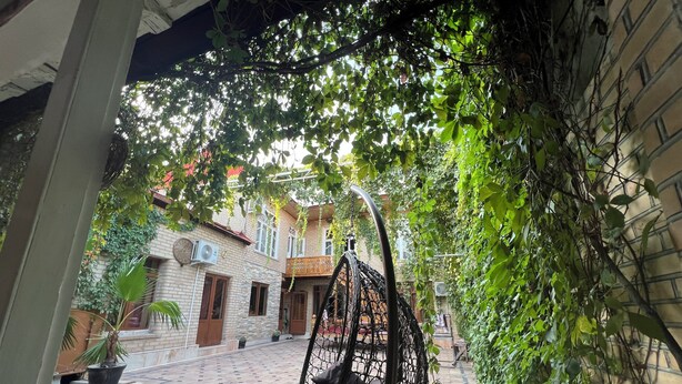 A hanging chair in a courtyard with a tiled floor, surrounded by greenery and a brick building. - Fayz Guest House (Samarkand)