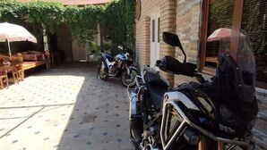 A tiled patio area with a row of parked motorcycles, a brick building, and a covered seating area with umbrellas. - Fayz Guest House (Samarkand)