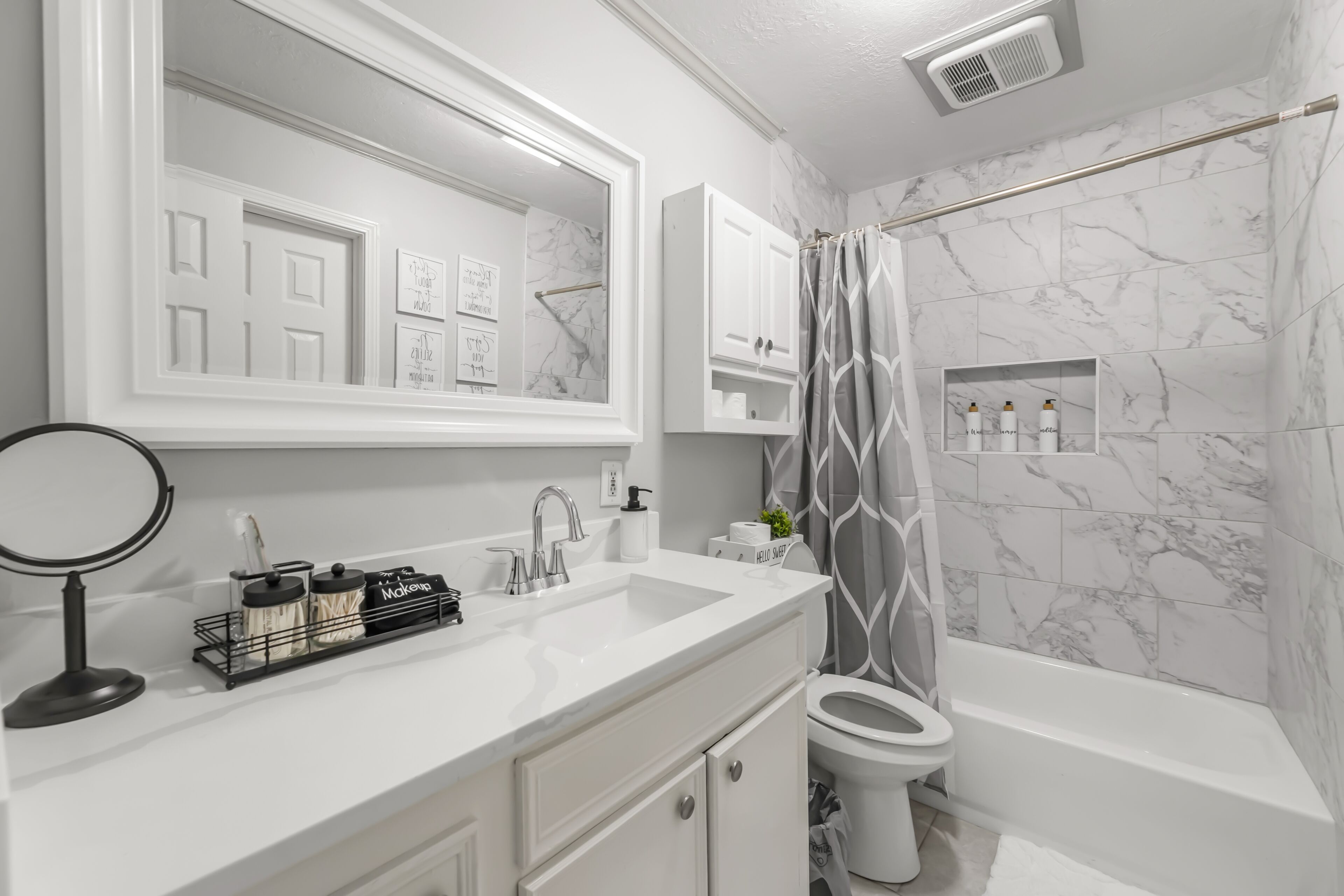 Une salle de bain moderne avec un meuble-lavabo blanc, un grand miroir, des toilettes et une baignoire.