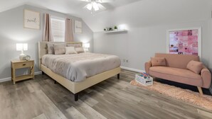 A bedroom with a bed, bedside tables, a ceiling fan, a pink sofa, and a wall with a picture frame. - A&M SPORTS DAY, POOL TABLE, AND BBQ (College Station)