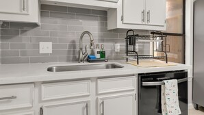 A modern kitchen with white cabinets, a stainless steel sink, and a black dishwasher. - A&M SPORTS DAY, POOL TABLE, AND BBQ (College Station)