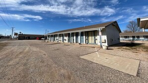 A motel with a row of rooms, a gravel parking lot, and a clear blue sky.