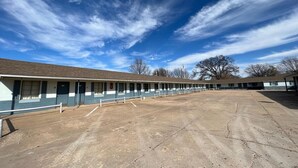 A row of motel rooms with a large parking lot in front.