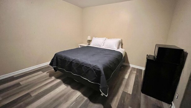 A bedroom with a bed, a nightstand, a TV stand, and a wooden floor.