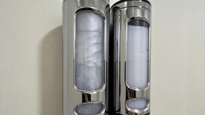 Two cylindrical objects with reflective surfaces and internal compartments, mounted on a wall.