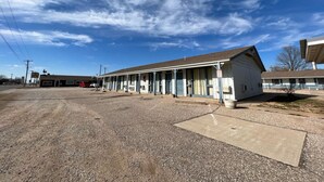 A motel with a row of single-story rooms, a parking lot, and a clear blue sky.