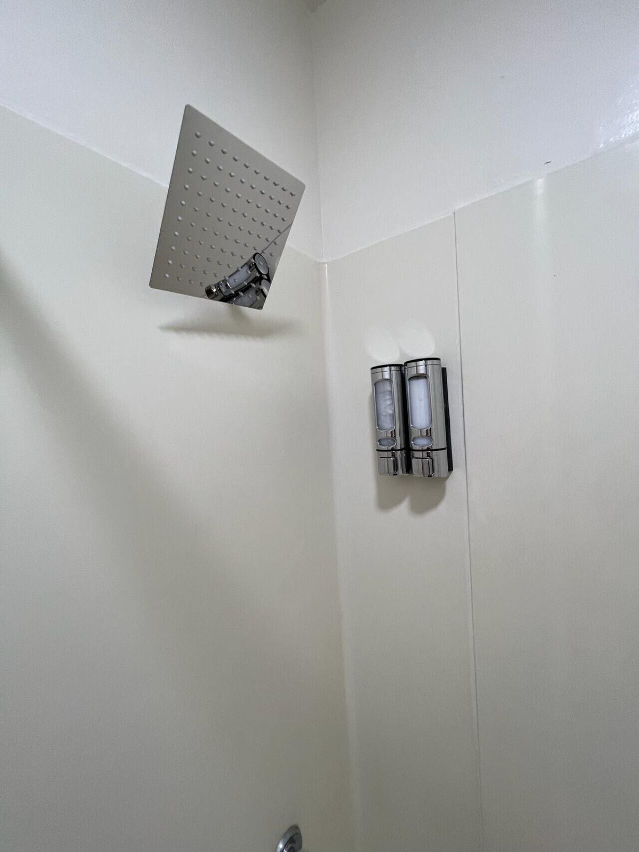 A shower area with a perforated ceiling panel and two wall-mounted fixtures.