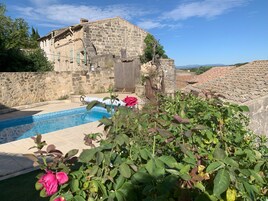 Um edifício de pedra com piscina, rodeado por vegetação e um céu claro.