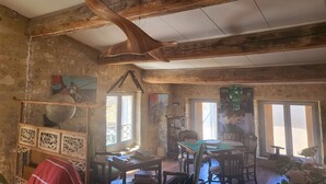 Una habitación rústica con vigas de madera a la vista, techo de madera, una mesa con libros, una silla y una ventana con vistas.