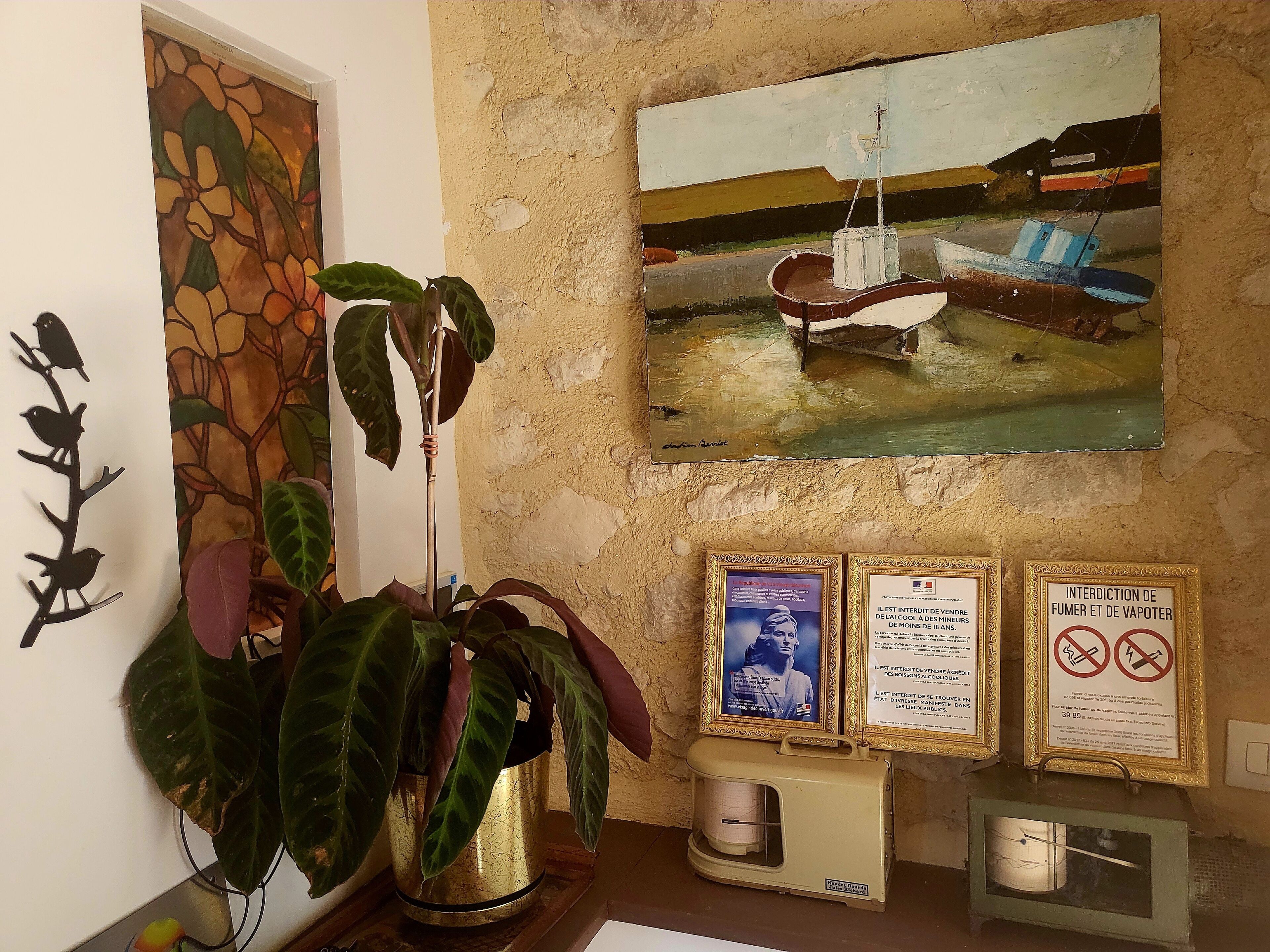 Una habitación con un cuadro grande de barcos, una planta en maceta y varios carteles enmarcados en la pared.