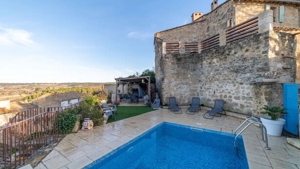 Un edificio de piedra con piscina, mobiliario exterior y vistas al campo.