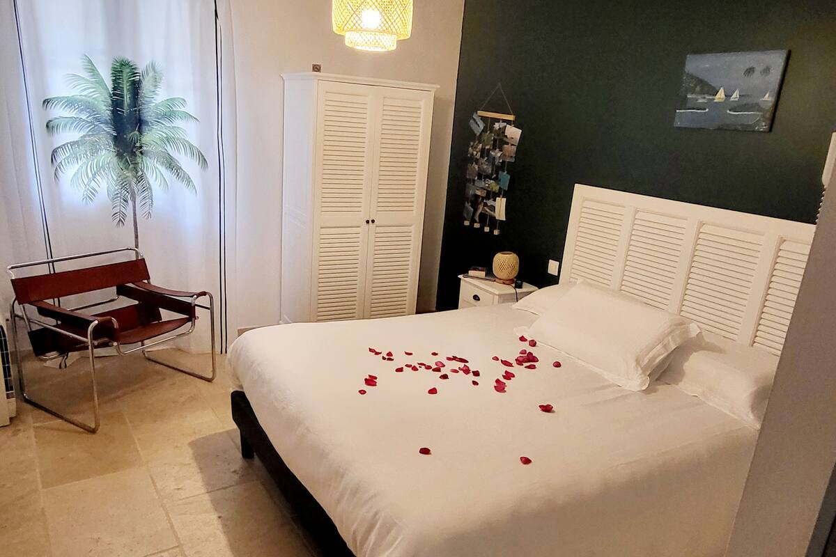 Un dormitorio con cama, mesita de noche, silla, armario y una pared con un cuadro.