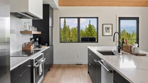 A modern kitchen with a large island, built-in appliances, and a view of trees and mountains through the windows. - Modern Mountain Escape | Hot Tub & Fireplace (Tabernash)