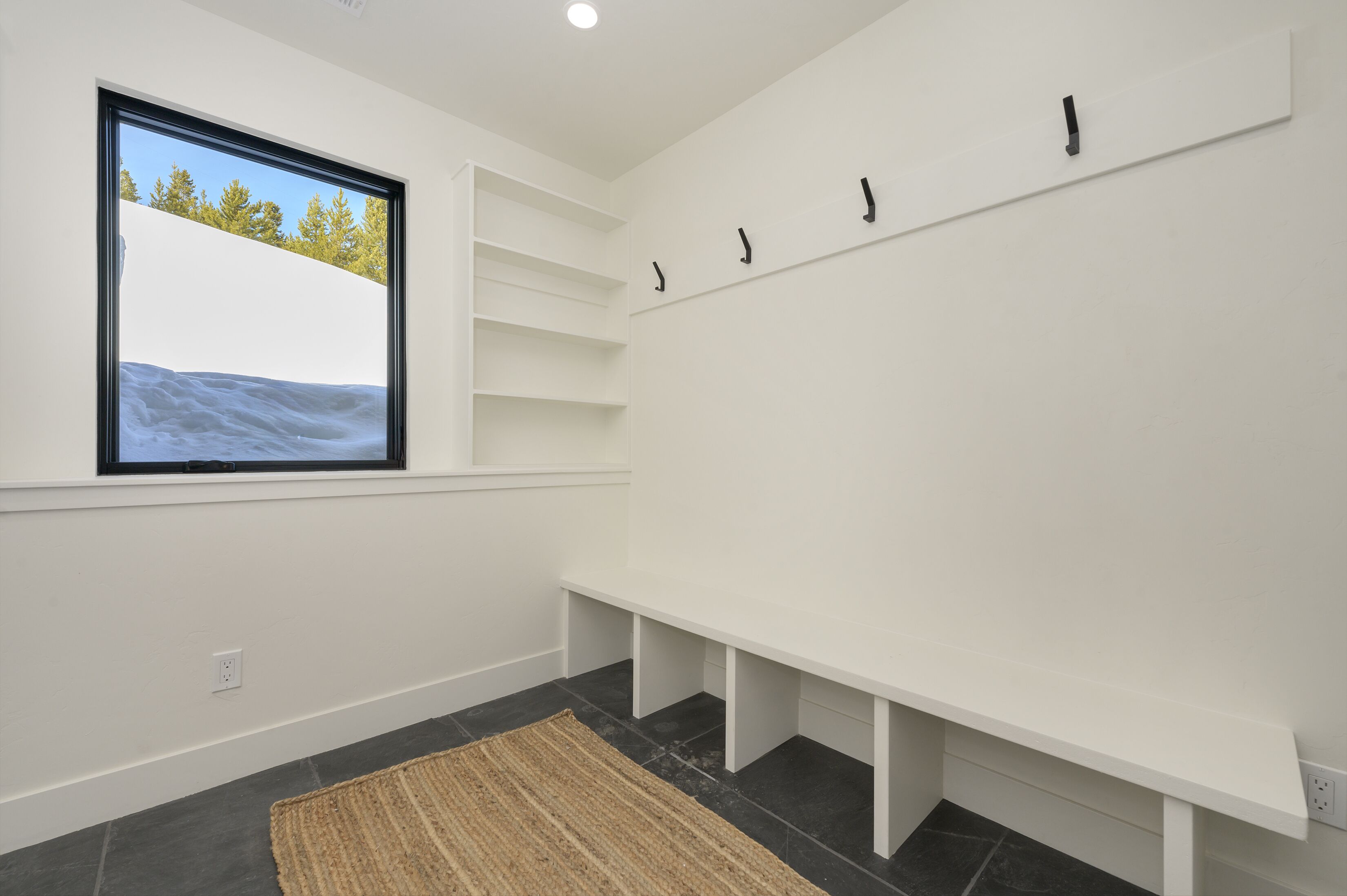 Une pièce dotée d’une grande fenêtre, d’un mur blanc avec un banc intégré et d’un porte-manteau fixé au mur.