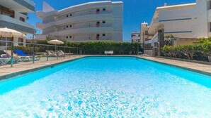 Una piscina con sillones de descanso y sombrillas, rodeada de edificios de varios pisos.