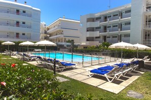 Zona de piscina con tumbonas y sombrillas, rodeada de edificios.