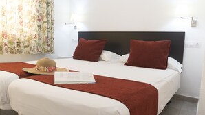 Habitación de hotel con dos camas, cada una con ropa de cama blanca y almohadas rojas. Hay un sombrero y un libro sobre la cama de la izquierda.