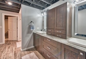 A modern bathroom with wooden cabinets, a large mirror, and a granite countertop. - Secluded Cabin Retreat – Your Escape to Nature! (Mancelona)