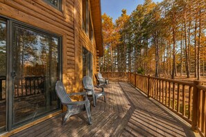 Une cabane en bois dotée d’une terrasse, de grandes fenêtres et offrant une vue sur une forêt.
