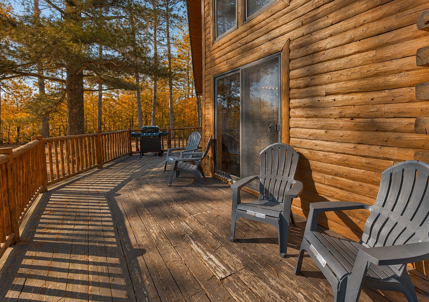A wooden deck with Adirondack chairs, a grill, and a glass door leading to a cabin.