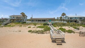 Una propiedad frente a la playa con un paseo de madera que lleva a un edificio con varias ventanas y una puerta.