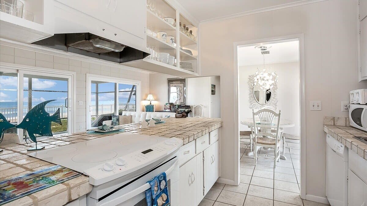A modern kitchen with white cabinetry, a large island, and a view of the sea.