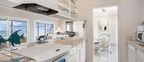 A modern kitchen with white cabinetry, a large island, and a view of the sea.