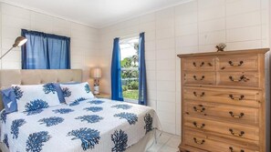 Une chambre à coucher avec un lit, une commode, une lampe et une fenêtre avec des rideaux.