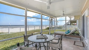 Un espace extérieur abrité, équipé d’une table et de chaises, d’un banc et offrant une vue sur la plage.