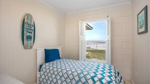 A bedroom with a bed, a window with shutters, a surfboard decoration, and a view of the outdoors.