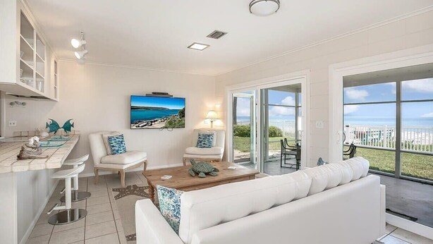 Una sala de estar moderna con un sofá blanco, dos sillones, una mesa de centro y un ventanal con vista al mar.