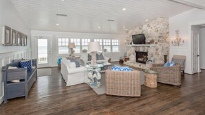 A spacious living room with a stone fireplace, comfortable seating, and a large window overlooking the ocean. - Sandy Chic Home with Oceanfront Deck & Fireplace (Ponte Vedra Beach)