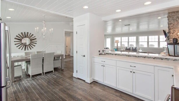 A modern kitchen with white cabinetry, a dining area with a chandelier, and a large window providing natural light. - Sandy Chic Home with Oceanfront Deck & Fireplace (Ponte Vedra Beach)