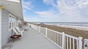 A covered porch with white railings, beach chairs, and a table, overlooking a beach. - Sandy Chic Home with Oceanfront Deck & Fireplace (Ponte Vedra Beach)