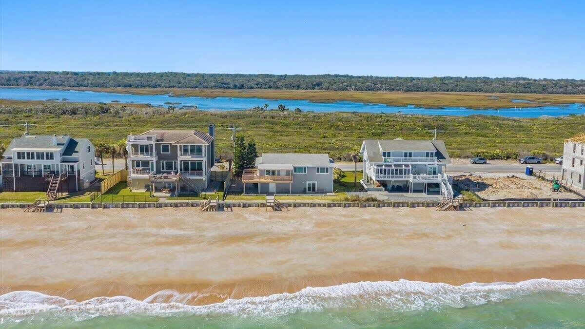 Een pand aan het strand met meerdere huizen, een zandstrand en uitzicht op de oceaan.