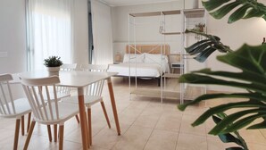A modern, well-lit room with a bed, a dining table with chairs, and a potted plant. - Mazi Apartments Havana (Mataró)