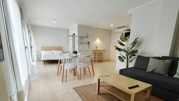 A modern living room with a sofa, a coffee table, and a dining area with chairs and a table. - Mazi Apartments Havana (Mataró)